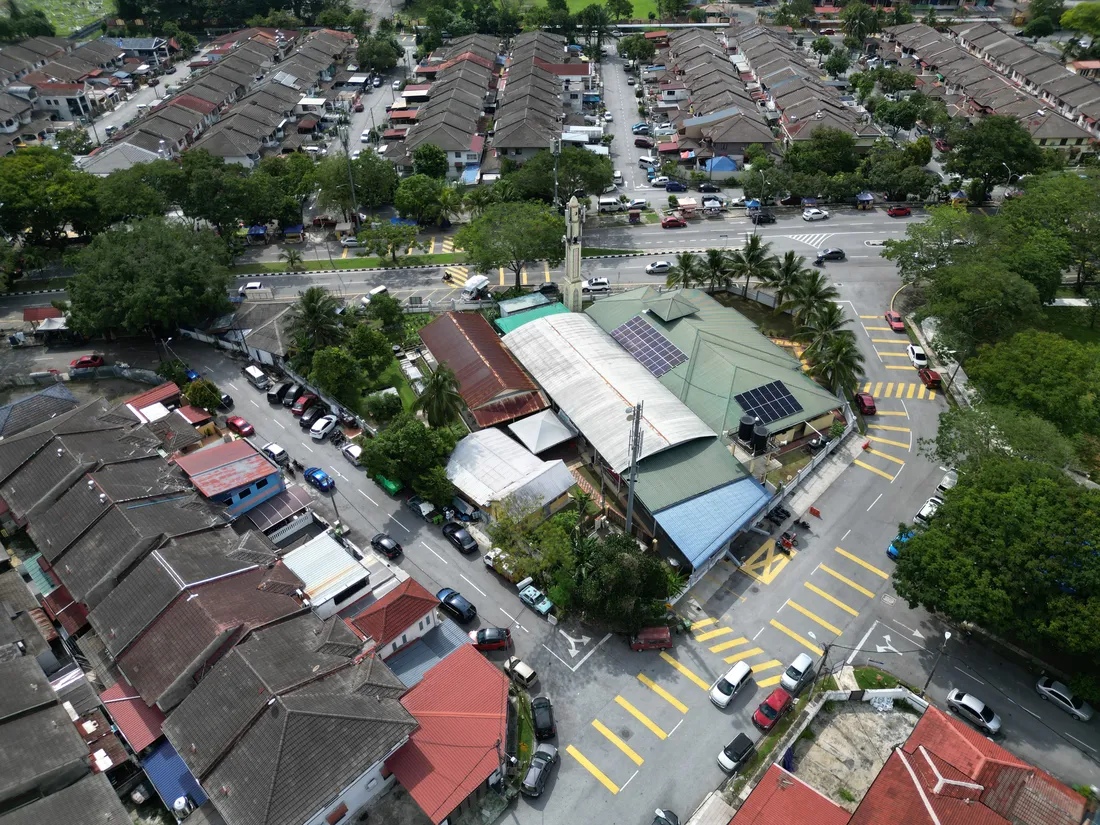 Aerial view of a mosque with a minaret, part of its roof fitted with solar panels, surrounded by a residential neighbourhood
