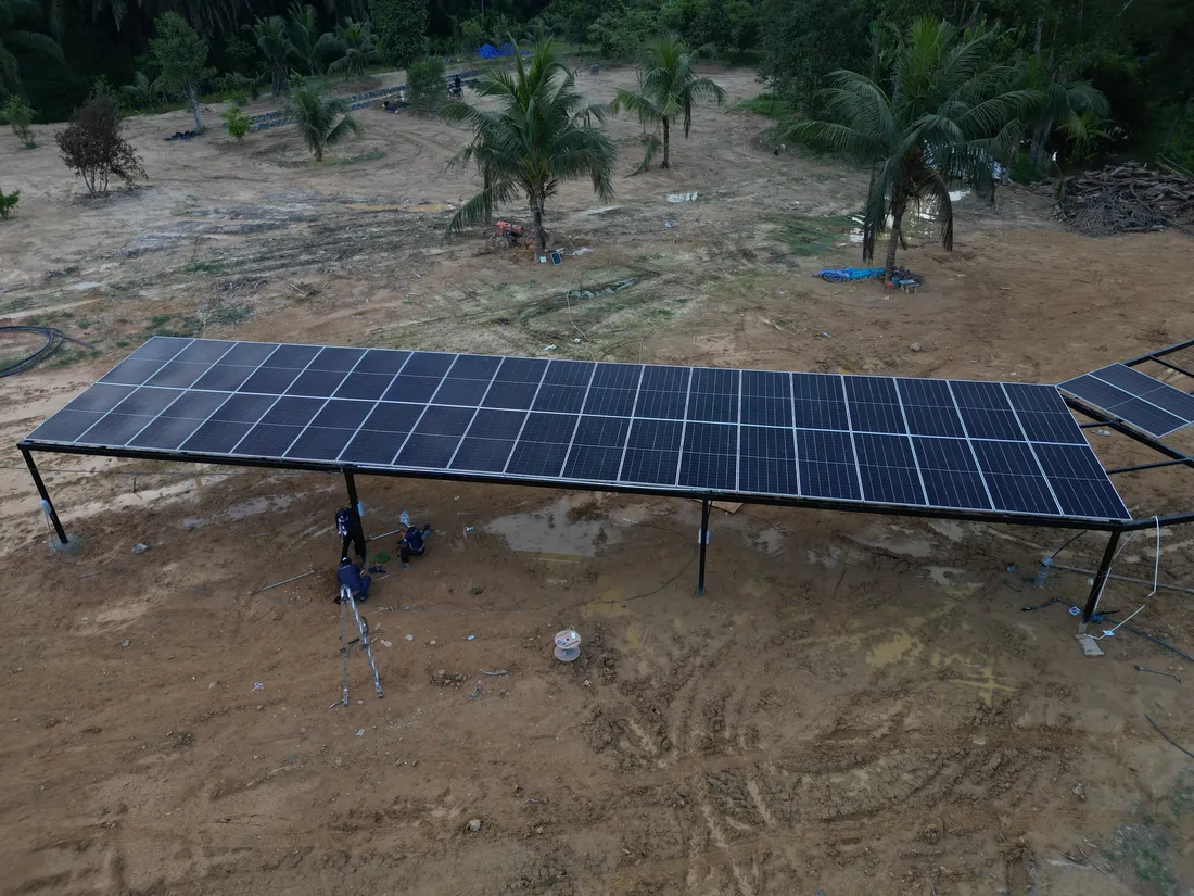 Aerial view of long rows of ground-mount solar panels under construction on cleared land